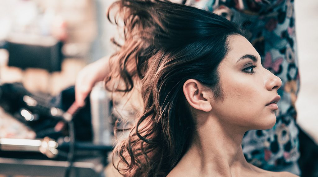 Hairdresser drying hair for young female