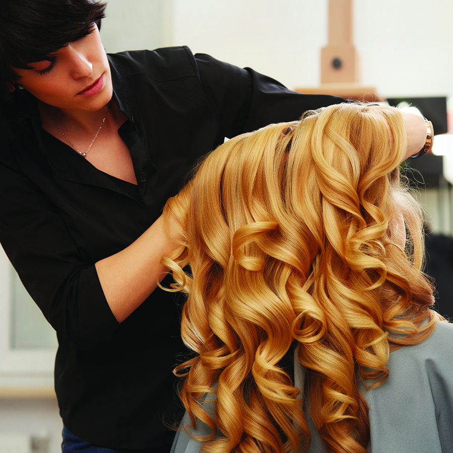 Blonde curly hair. Hairdresser doing hairstyle for young woman in salon